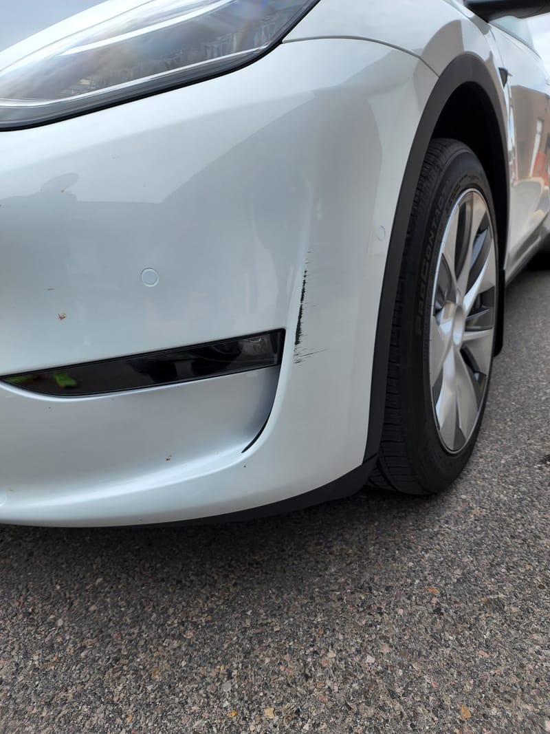 Close-up of a black scrape running across the front bumper corner of a white Tesla Model Y