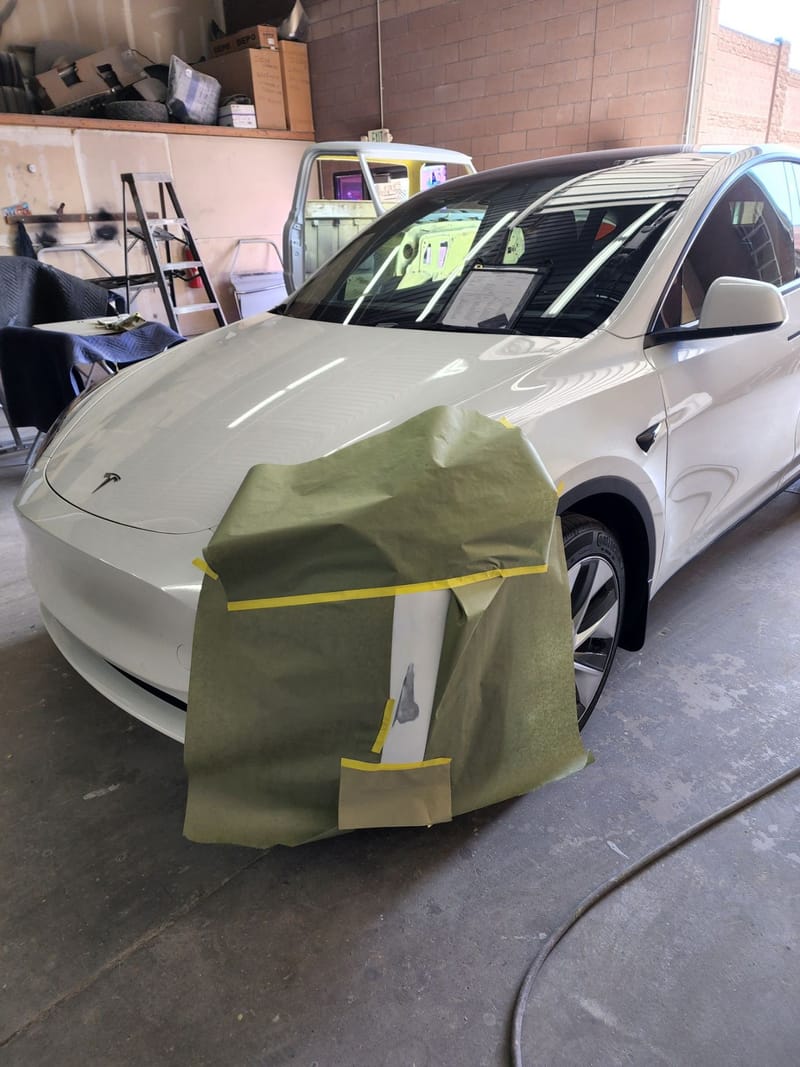Close-up of masking paper and tape covering the front corner of the Model Y before refinishing
