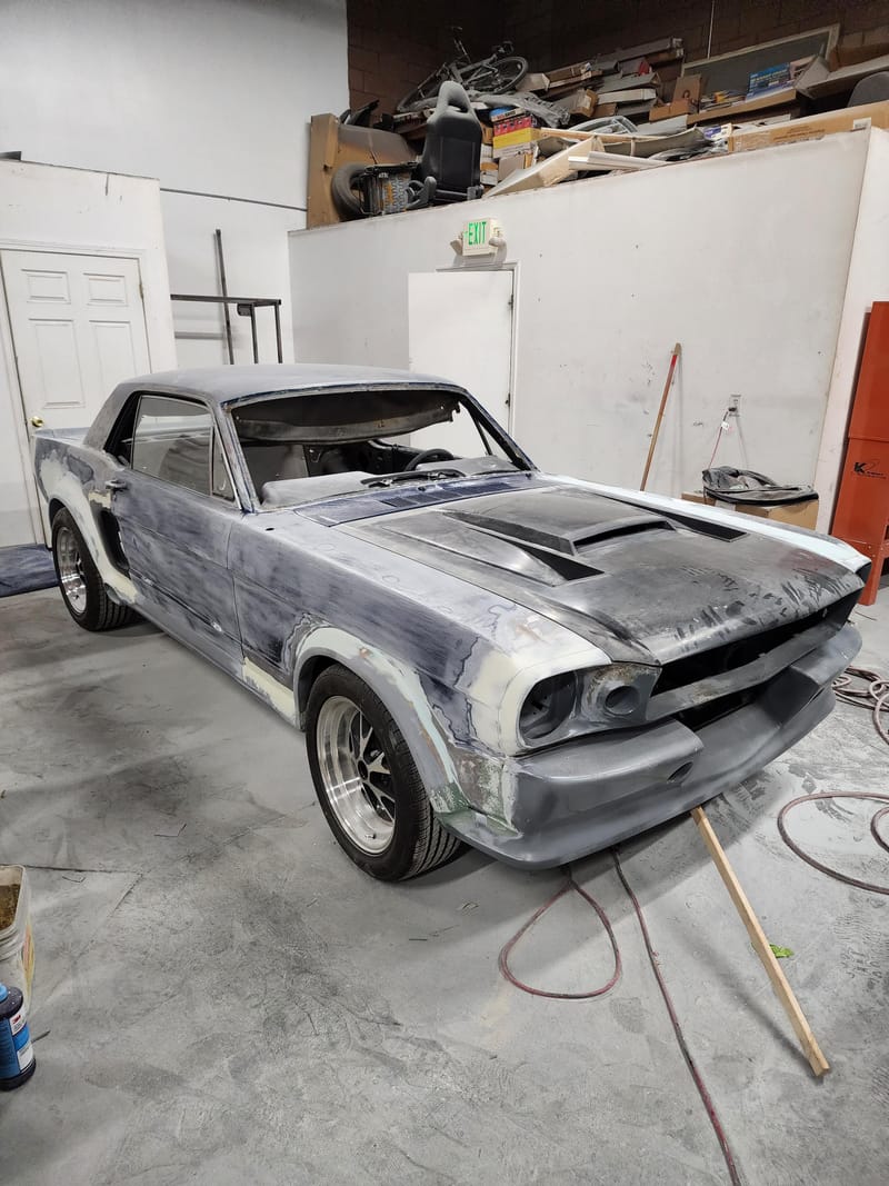 A classic Mustang coupe mid-restoration in the shop, panels in filler and primer
