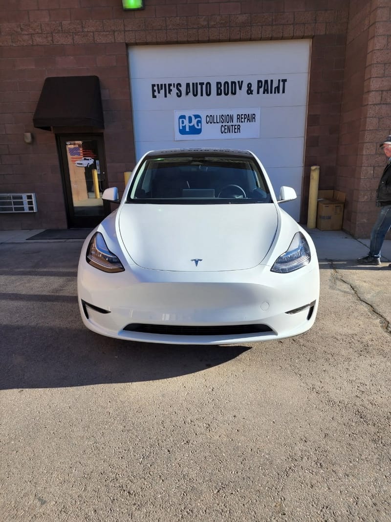 The finished Model Y outside the shop door, below the Evie's Auto Body & Paint and PPG Collision Repair Center signs